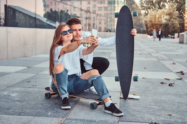 Retrato de jovem casal vestido com roupas da moda se divertindo enquanto faz uma selfie juntos ao ar livre . — Fotografia de Stock