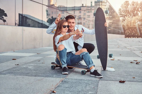 Retrato de pareja joven vestida con ropa de moda divirtiéndose mientras hace una selfie juntos al aire libre . — Foto de Stock