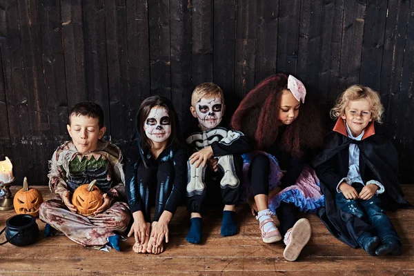 Halloweenfest med gruppen barn som sitter ihop på ett trägolv i ett gammalt hus. Halloween-konceptet. — Stockfoto