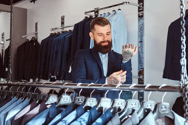 微笑 tattoed 男性与时尚的胡子和头发穿着优雅西装站在男装店. — 图库照片