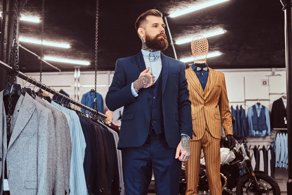Assistente de loja barbudo elegantemente vestido com pé perto de manequim na loja de moda masculina . — Fotografia de Stock