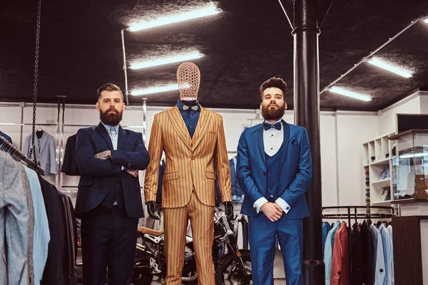 Due commesse elegantemente vestite posano vicino al manichino nel negozio di abbigliamento maschile . — Foto Stock