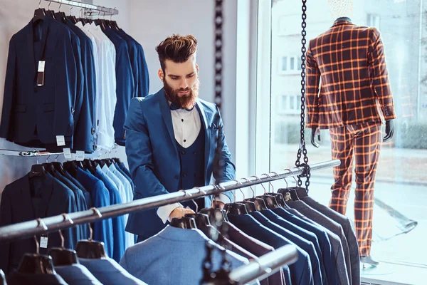 Skäggiga butiksbiträde klädd i blå elegant kostym arbetar i herrkläder store. — Stockfoto