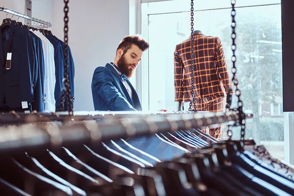 Γενειοφόρος κατάστημα Βοηθός ντυμένος με μπλε κομψό κοστούμι, εργάζεται στο κατάστημα Ανδρικά ενδύματα. — Φωτογραφία Αρχείου