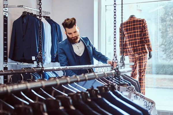 Skäggiga butiksbiträde klädd i blå elegant kostym arbetar i herrkläder store. — Stockfoto