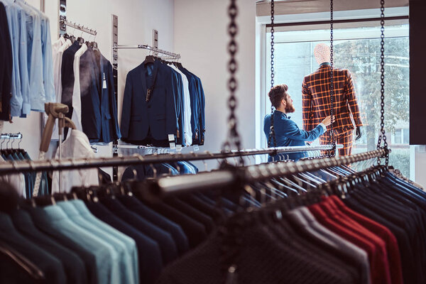 Stylish bearded seller care about suit on a mannequin in a menswear store.