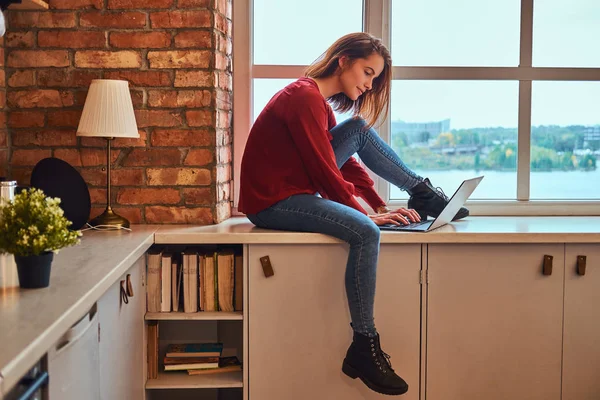 Jovem menina estudante bonita sentado com laptop no peitoril da janela no dormitório do estudante . — Fotografia de Stock