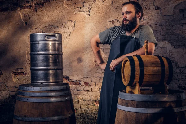 Cervecero en delantal de pie cerca de barriles en la antigua fábrica de cerveza . — Foto de Stock