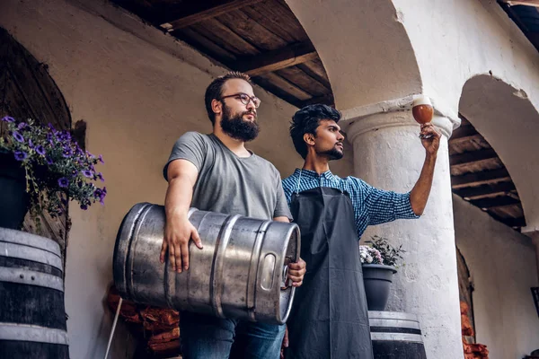 Dois cervejeiros em avental de pé ao ar livre verificando a qualidade da bebida fermentada na fábrica de cervejaria . — Fotografia de Stock