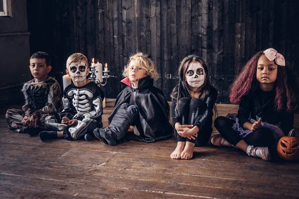 Halloweenfest med gruppen barn som sitter ihop på ett trägolv i ett gammalt hus. Halloween-konceptet. — Stockfoto