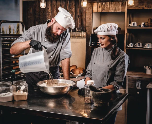 Chef-kok mengt de ingrediënten voor het deeg. Chef-kok onderwijs zijn assistent te bakken van brood in de bakkerij. — Stockfoto