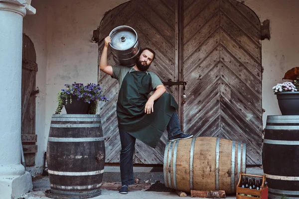 Cervecero en delantal sostiene barril con cerveza artesanal en fábrica de cerveza . — Foto de Stock