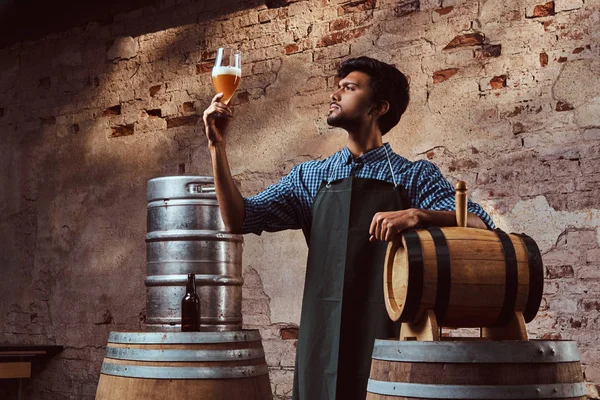 Cervecero experto en delantal de pie cerca de barriles que comprueban la calidad de la bebida elaborada en la fábrica de cerveza . — Foto de Stock