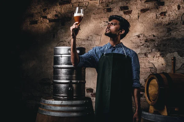 Cervejeiro especialista em avental de pé perto de barris verificando a qualidade da bebida fermentada na fábrica de cervejaria . — Fotografia de Stock