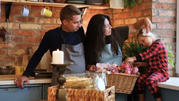 Familia en estilo loft cocina por la mañana. Madre sostiene una canasta con flores y habla con su hijita . — Vídeo de stock