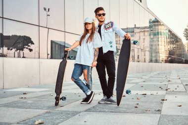 Kaykaylar gökdelen yakınındaki ile poz trendy elbise giymiş çekici genç çift.