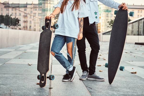裁剪照片的时髦打扮年轻夫妇摆在摩天大楼附近的滑板. — 图库照片