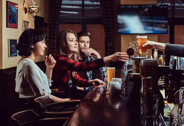 Giovani amici multirazziali al bar. barman che dà un bicchiere di birra al cliente nel pub . — Foto Stock