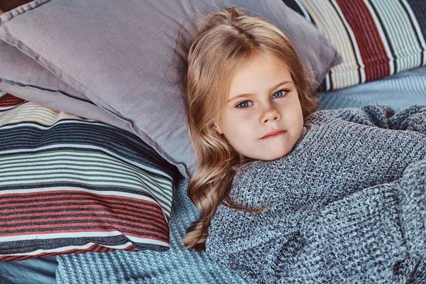 Retrato de cerca de una niña en suéter caliente acostada en la cama . — Foto de Stock