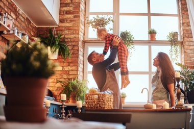 Mutlu baba küçük kızı anne yakınındaki sabah loft tarzı mutfakta ayakta iken ellerinde tutan.