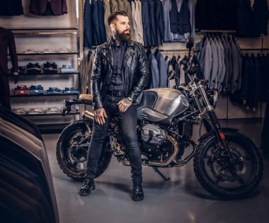 Vahşi erkek erkek giyim mağazasında bir retro spor motosiklet üzerinde eğilerek siyah ceket giymiş.