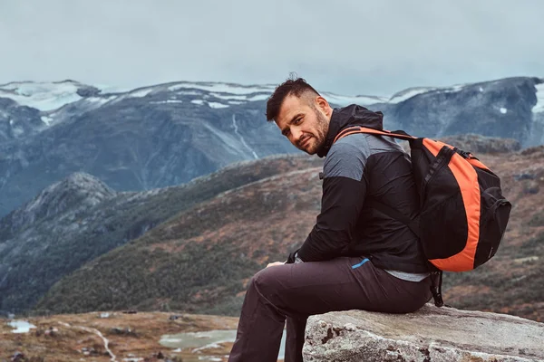Un bell'uomo siede su una roccia sullo sfondo di un bellissimo paesaggio montano in Norvegia . — Foto Stock