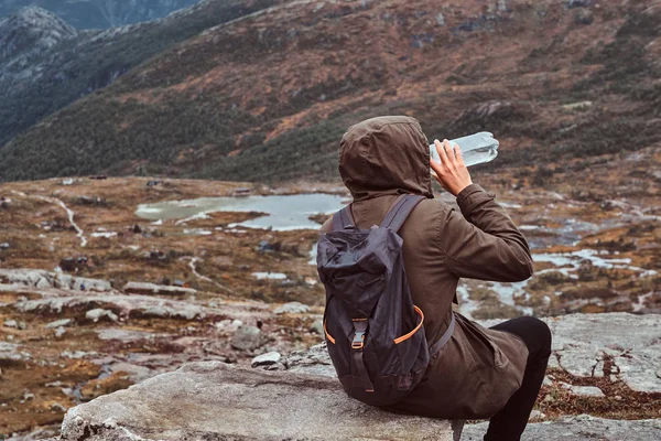 Vista trasera de un turista que bebe agua y se sienta en una roca en el fondo de un hermoso paisaje de montaña . —  Fotos de Stock