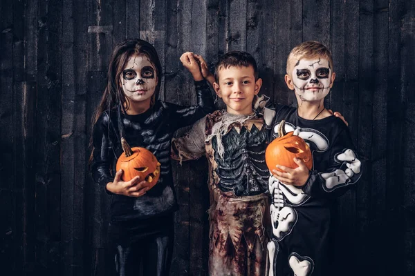 Tres niños multirraciales en trajes de miedo posando con calabazas en una casa vieja . —  Fotos de Stock