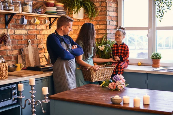 Family in loft style kitchen at morning. Mother hold a basket with flowers and talking with her little daughter.