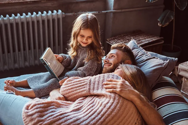 Mãe, pai e filha lendo o livro de histórias juntos enquanto estavam deitados na cama . — Fotografia de Stock