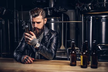 Indie bira sayacında bar, otururken zanaat bira şişesiyle şık sakallı bisikletçinin giymiş siyah deri ceket tutar.