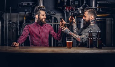 Two stylish bearded hipsters friends drinking beer together at indie brewery. clipart