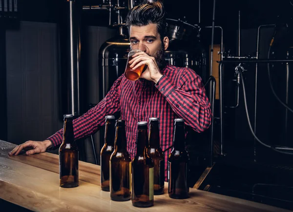 Hipster man met stijlvolle baard en haren drinken bier aan de bar zitten teller in indie brouwerij. — Stockfoto