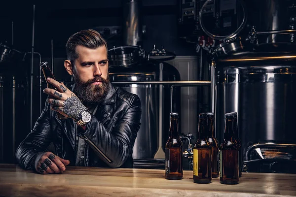 Elegante motorista barbudo vestido chaqueta de cuero negro sentado en el mostrador del bar en la fábrica de cerveza indie . —  Fotos de Stock