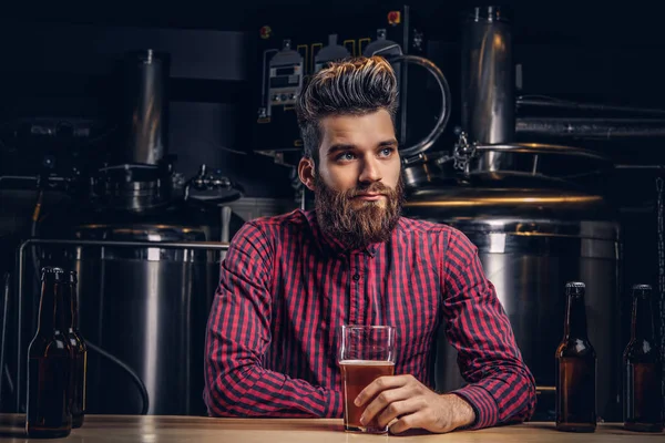 Hipster man met stijlvolle baard en haren drinken bier aan de bar zitten teller in indie brouwerij. — Stockfoto