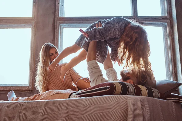 Mãe, pai e filha na cama. Pai brincando com filha adorável no quarto . — Fotografia de Stock