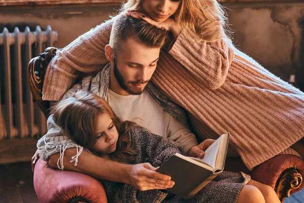 Reunião familiar. Mãe, pai e filha lendo livro de histórias juntos sentados no sofá. Conceito de família e paternidade . — Fotografia de Stock