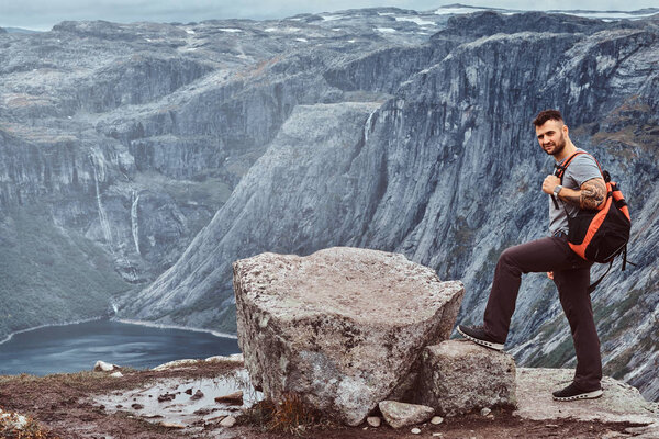 Tourist stands on the peak of the mountain with an amazing view of the Norwegian fjord.