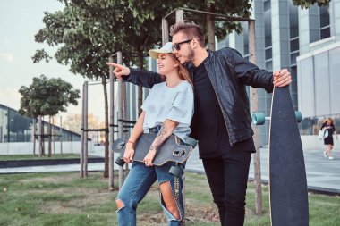 Trendy genç çift ayakta birlikte gökdelen yakınındaki küçük bir çimenlikte giyinmiş.