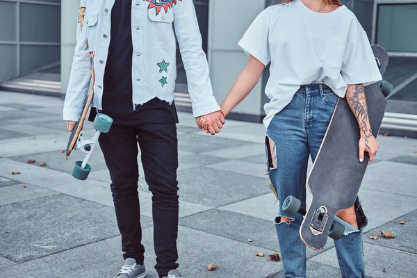 Cropped photo of young trendy dressed skaters hold hands while standing near skyscraper. — Stock Photo, Image
