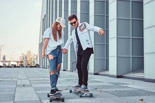 Glückliches junges Paar hat Spaß beim Skateboardfahren auf einer modernen Straße. — Stockfoto