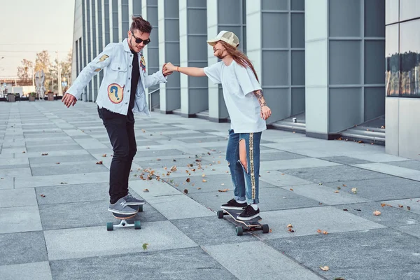 Gelukkige jonge paar plezier tijdens het rijden skateboards op een moderne straat. — Stockfoto