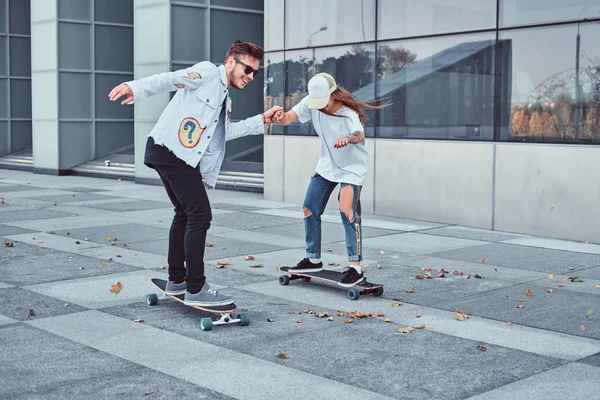 Glada unga par ha kul medan du kör skateboard på en modern gata. — Stockfoto