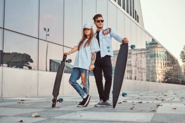 Kaykaylar gökdelen yakınındaki ile poz trendy elbise giymiş çekici genç çift.