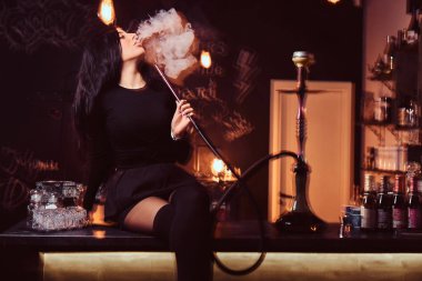 Seksi esmer kız baştan çıkarıcı siyah giysili bir gece kulübü ya da bar counter üzerinde otururken bir nargile içiyor.