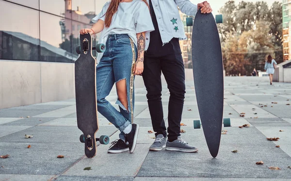 Foto recortada de una pareja joven vestida de moda posando con monopatines cerca de un rascacielos . — Foto de Stock