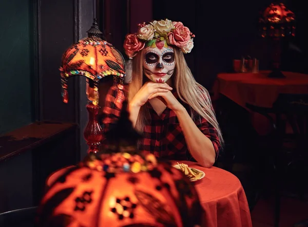 Young blonde girl with undead makeup in flower wreath eating nachos at a mexican restaurant. — Stock Photo, Image