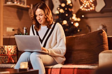 Kadın Noel Noel zamanda dekore edilmiş oda içinde internet üzerinden alışveriş yapma kanepede rahatlatıcı.