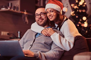 Laptop - kadın erkeğini sarılma ve kameraya bakarak Santa şapka sevimli sevimli bir çiftle portresi.