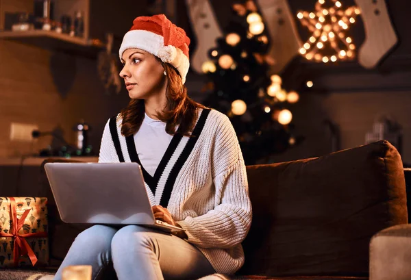Женщина отдыхает на диване делает рождественские покупки в Интернете в украшенном номере в Рождество время . — стоковое фото